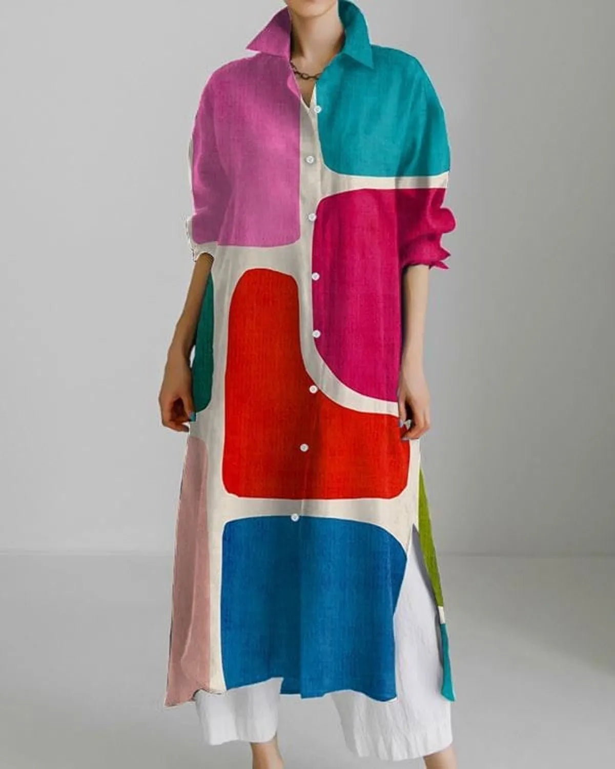 A long shirt dress with a multicolor geometric pattern, featuring a collar, buttons, and a uneven hemline.